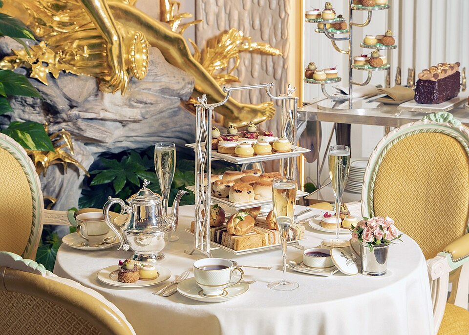 A round table laid for afternoon tea with a tiered stand, teapot, cups and saucers
