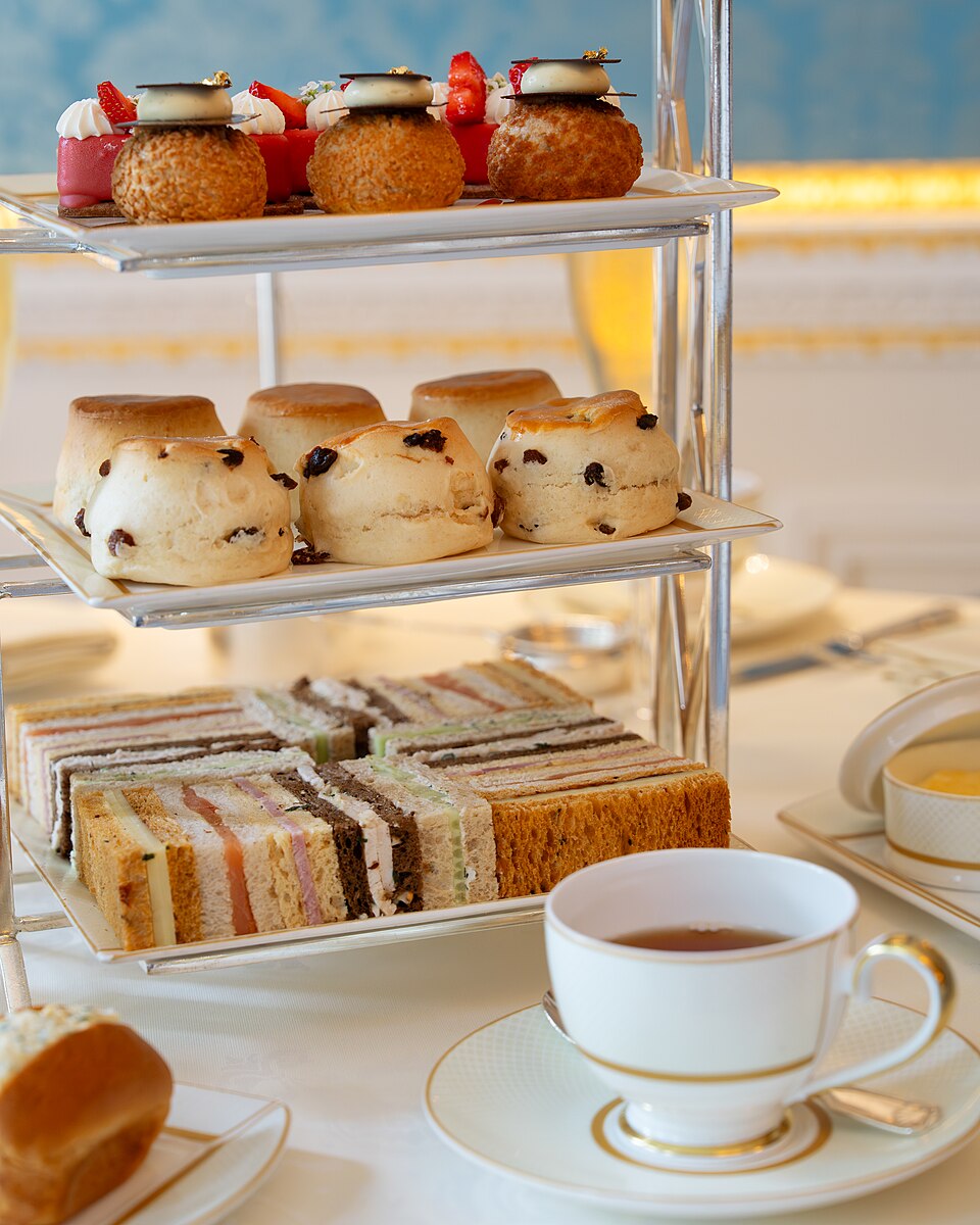 A tiered cake stand with afternoon tea sandwiches, scones and cakes