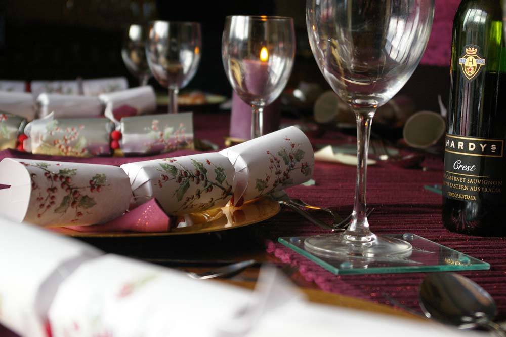 A Christmas table set with crackers, wine glasses and a bottle of wine