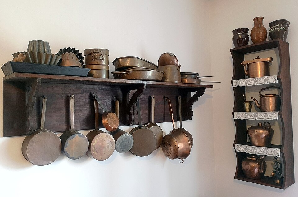 Copper pans hanging from a wall rack with shelves above