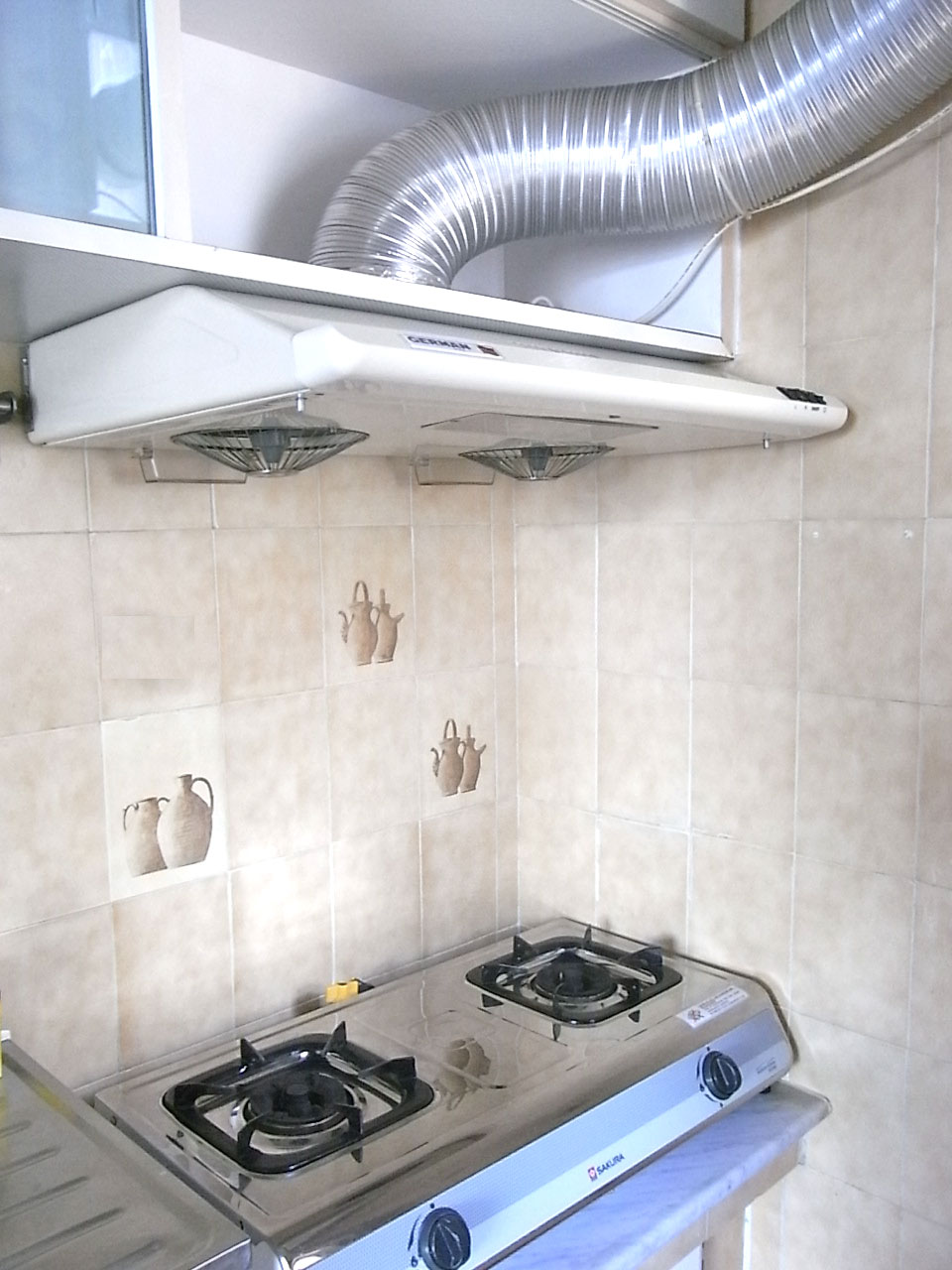 A slimline extractor hood above a two-burner gas hob, with its duct pipe exposed