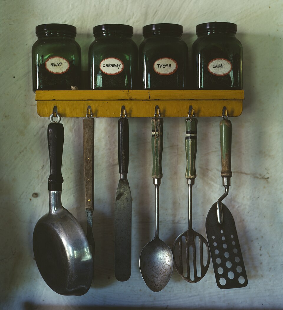 Kitchen utensils hanging from a rail below a spice rack