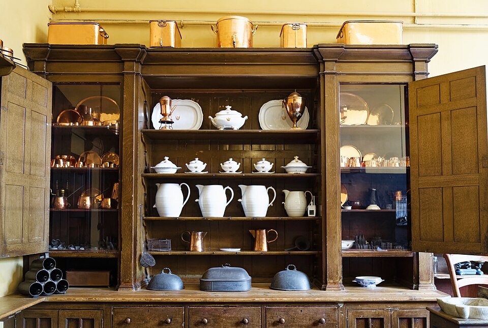 A tall freestanding kitchen cupboard at Charlecote Park, filled with china and copper