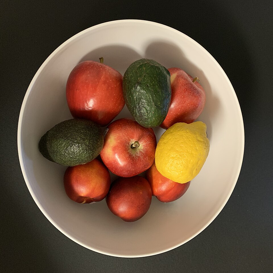 A bowl of apples, lemons and avocados on a kitchen counter