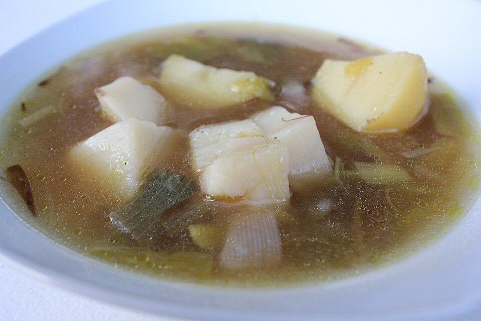A bowl of leek and potato soup in a clear broth