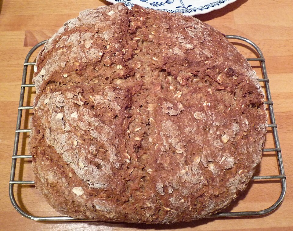 A round loaf of brown soda bread cooling on a wire rack
