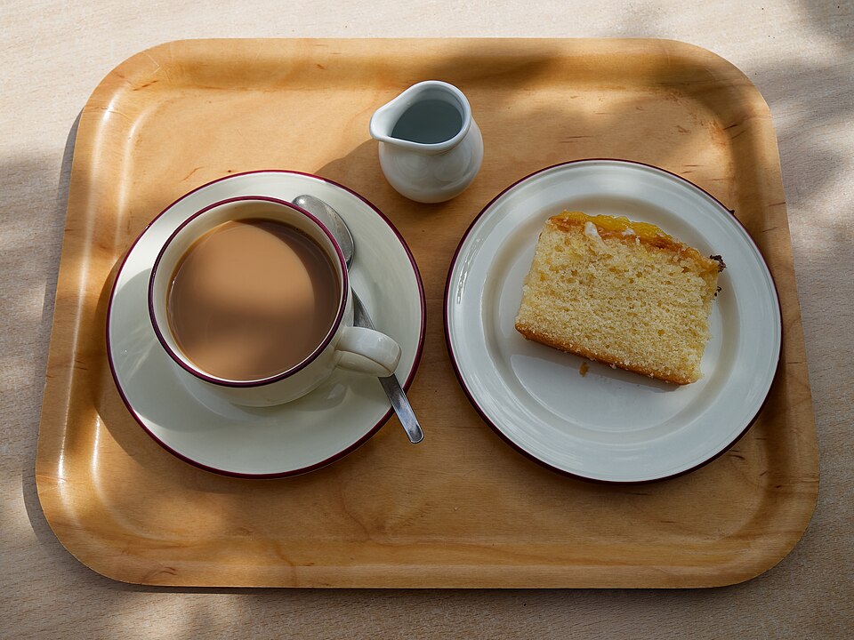A slice of lemon drizzle cake served with a cup of tea