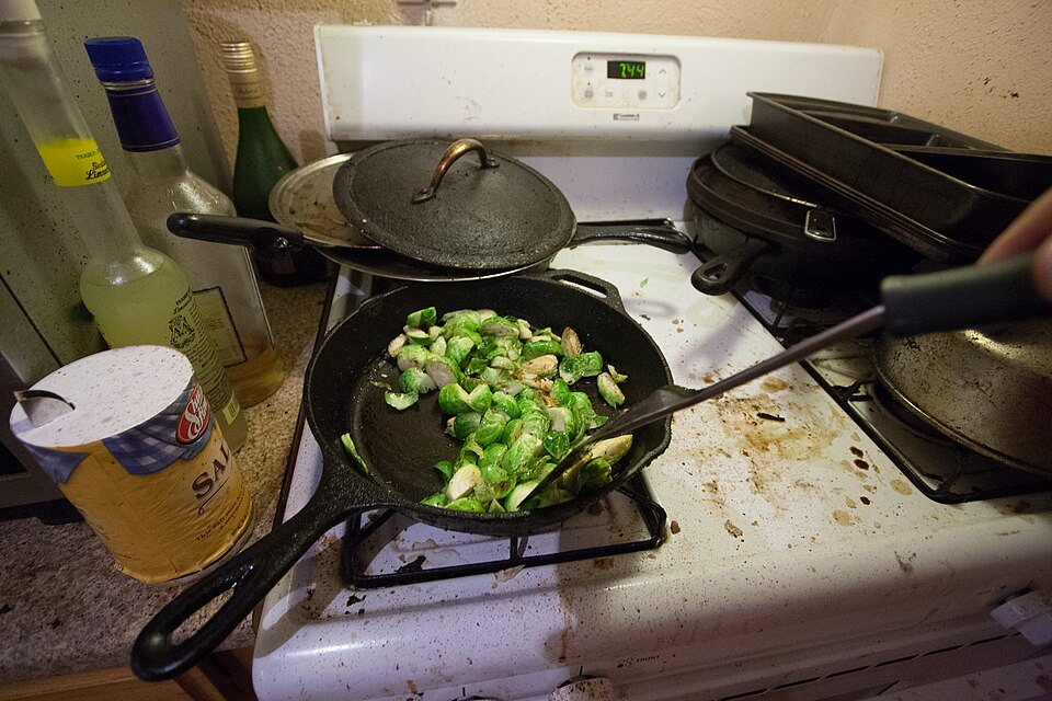 Brussels sprouts and bacon being fried in a cast-iron pan
