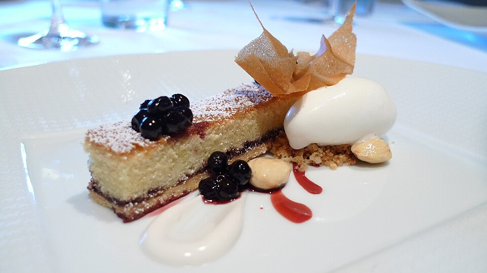 A slice of Bakewell tart served with cream and berries