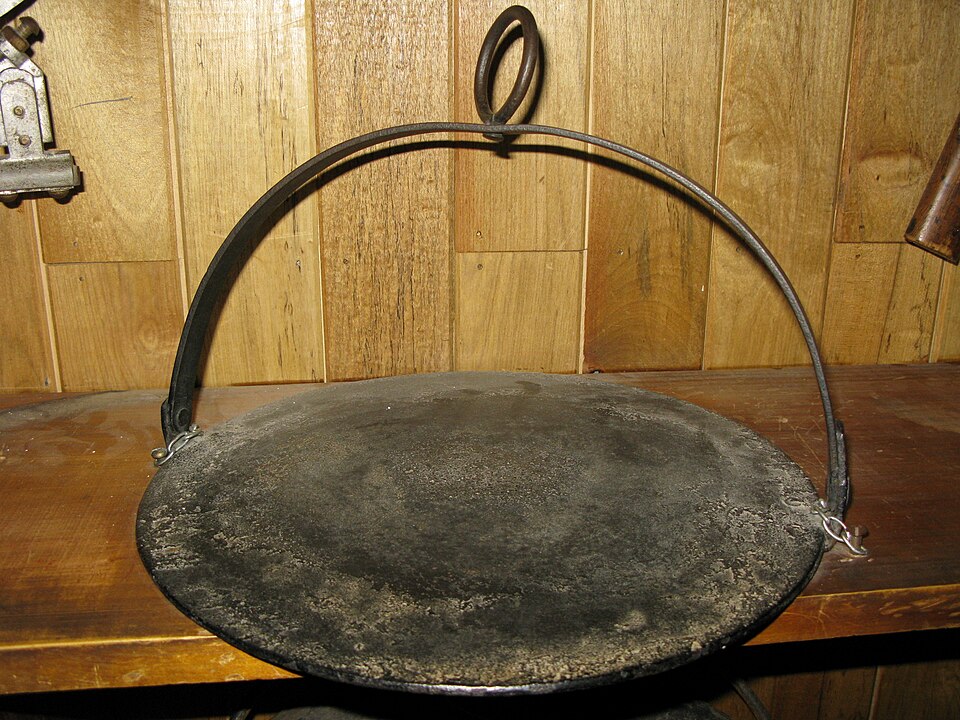 A traditional flat iron girdle (griddle) with a hoop handle