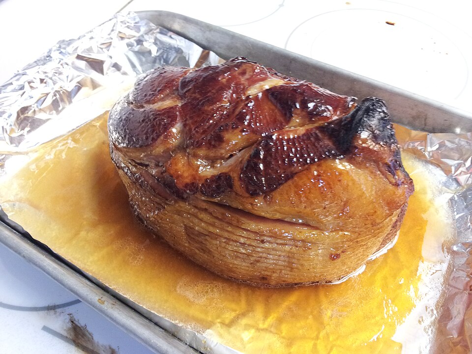 A glazed ham in a foil-lined roasting tin