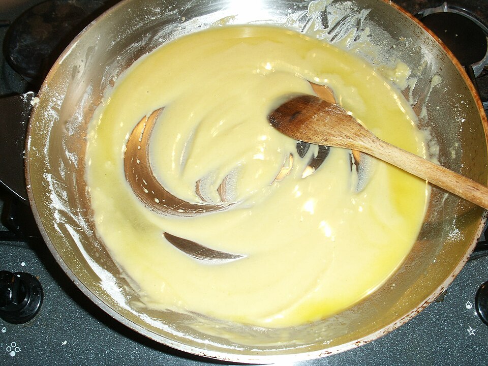 A roux of butter and flour being stirred in a pan