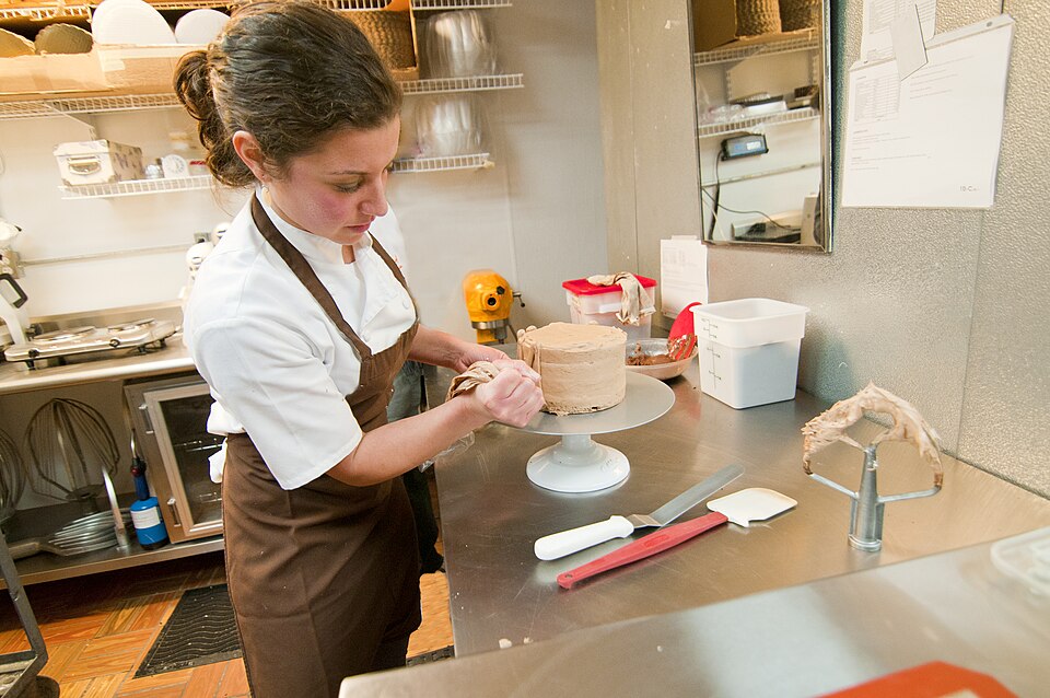 A pastry cook icing a cake on a turntable