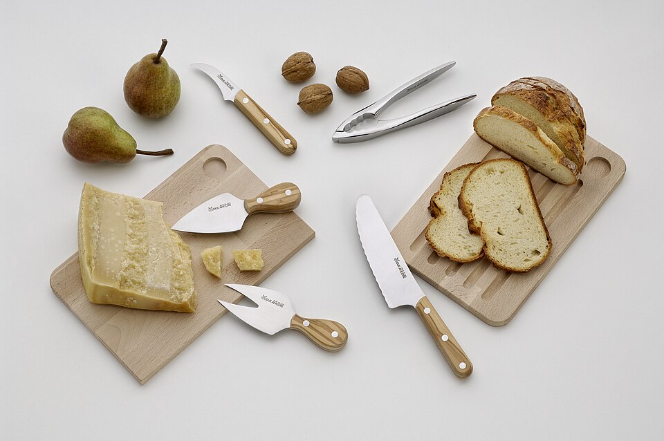 A cheese board with several cheese knives, bread and pears