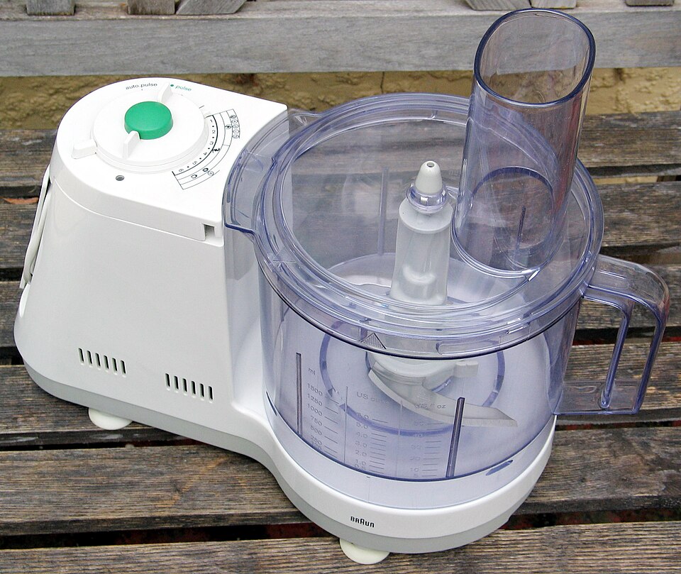 A white food processor with a clear bowl and feed tube
