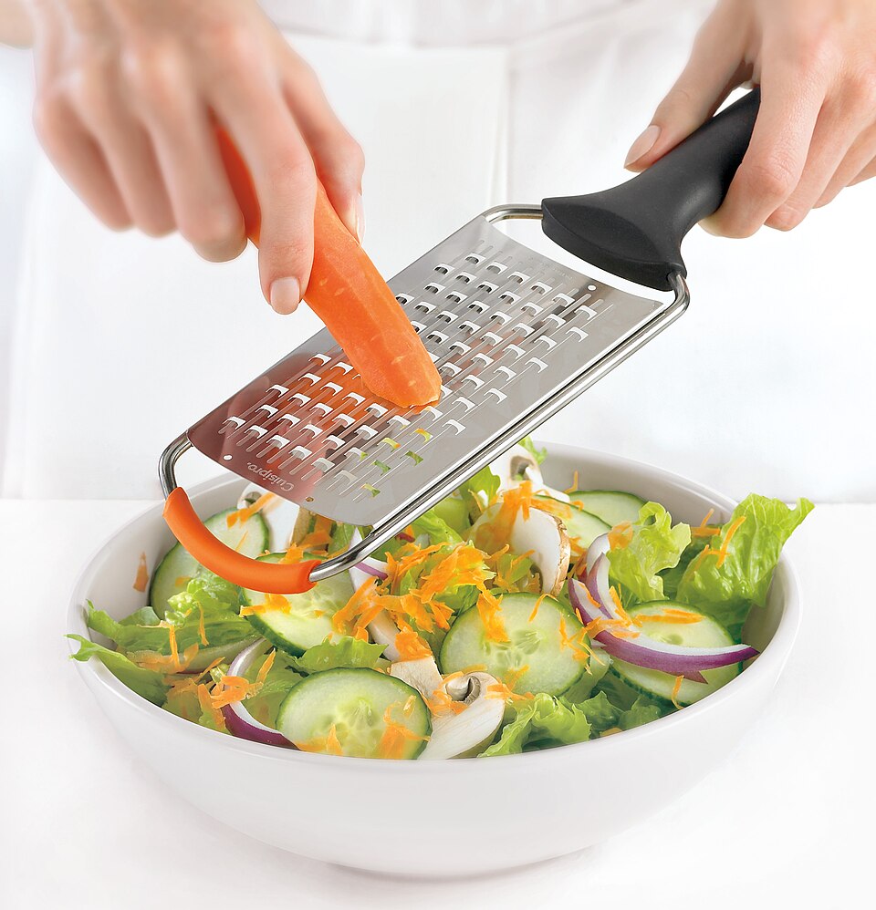 Grating carrot over a salad with a flat grater