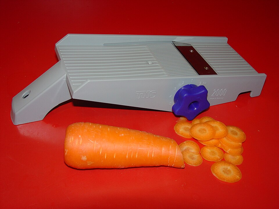 A mandoline slicer with a carrot cut into thin rounds
