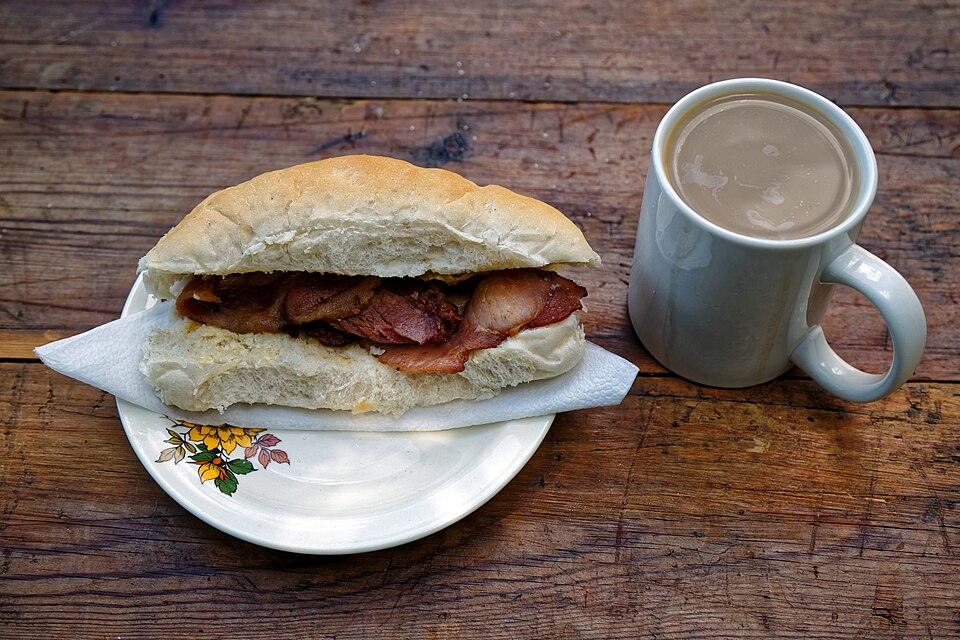 A bacon roll beside a mug of tea