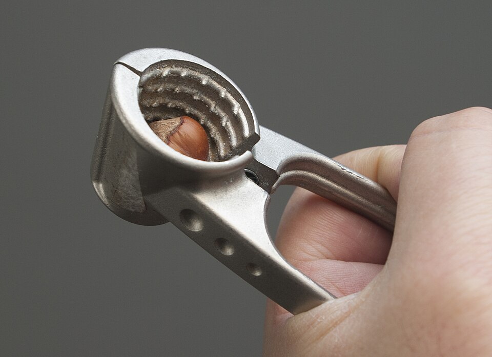 A hand cracking a hazelnut in a metal nutcracker