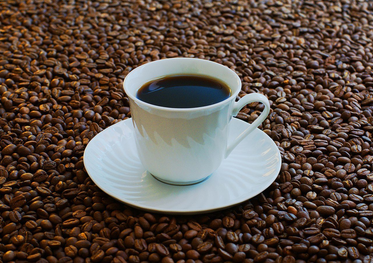 Cup of coffee surrounded by roasted coffee beans