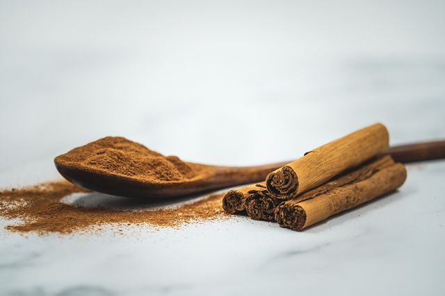 Ground cinnamon on a wooden spoon beside cinnamon sticks