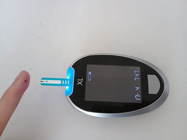 Finger with a blood drop next to a glucose meter and test strip
