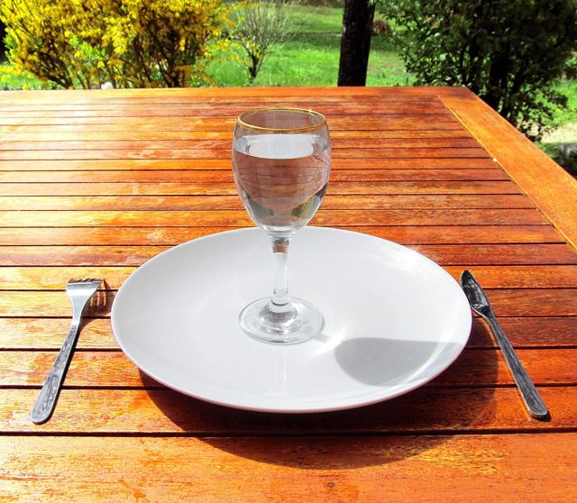Glass of water on an empty plate on a garden table